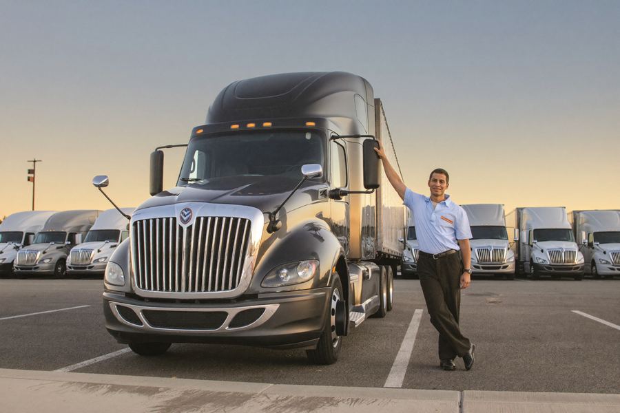 A refreshed truck driver stretching beside the cab of a parked semi-truck in a clean secure lot at dawn
