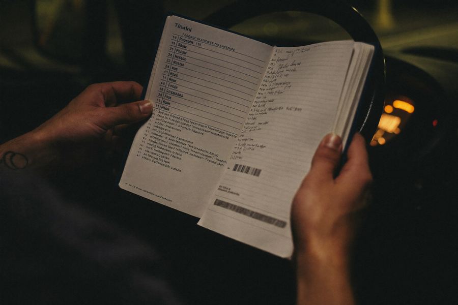 A driver's hands holding a paper logbook and a fuel receipt inside a dim truck cab at night